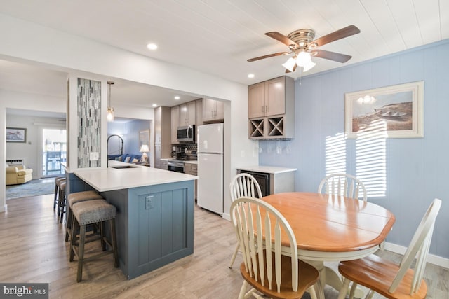 kitchen with sink, a kitchen breakfast bar, ceiling fan, stainless steel appliances, and light wood-type flooring