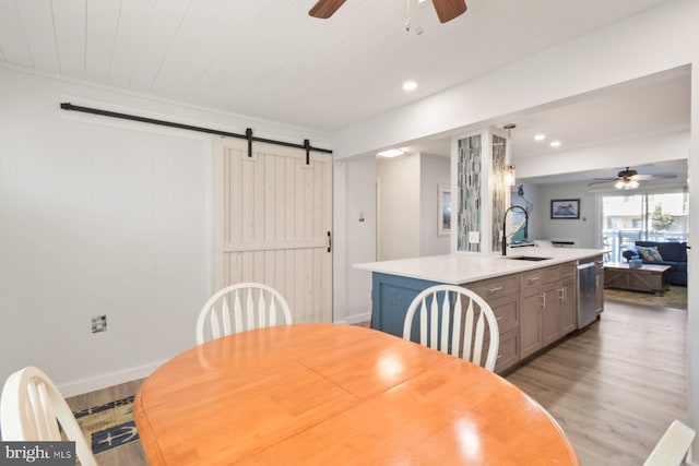 dining area with ceiling fan, a barn door, sink, and light hardwood / wood-style floors