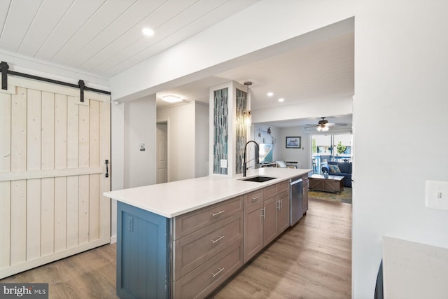 kitchen with sink, dishwasher, light hardwood / wood-style floors, a center island with sink, and a barn door