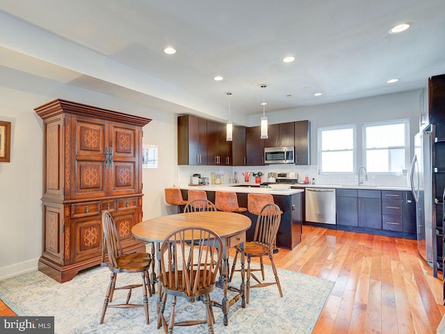 kitchen featuring backsplash, light hardwood / wood-style floors, hanging light fixtures, a breakfast bar area, and stainless steel appliances