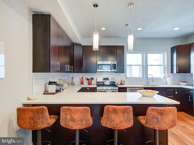 kitchen with decorative light fixtures, kitchen peninsula, sink, appliances with stainless steel finishes, and a kitchen breakfast bar