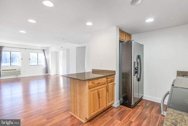 kitchen featuring a wall unit AC, stove, dark wood-type flooring, stainless steel fridge with ice dispenser, and dark stone counters