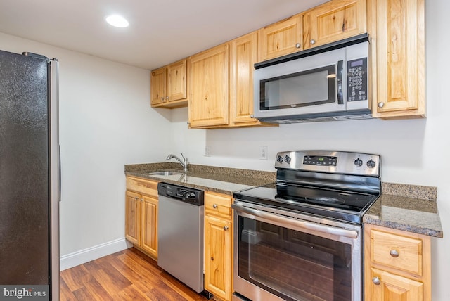 kitchen featuring hardwood / wood-style flooring, stainless steel appliances, light brown cabinetry, dark stone counters, and sink