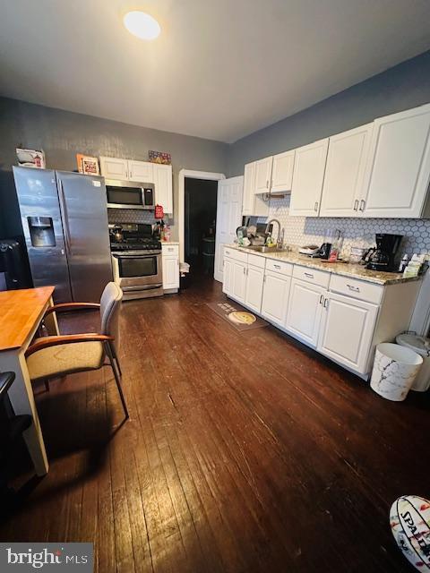 kitchen with sink, light stone countertops, stainless steel appliances, white cabinets, and dark hardwood / wood-style flooring