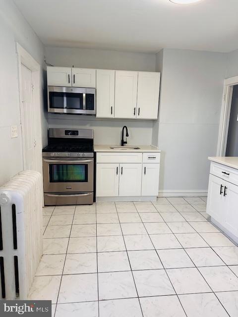 kitchen with sink, white cabinets, radiator heating unit, and stainless steel appliances