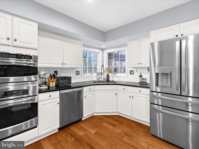 kitchen featuring sink, white cabinetry, appliances with stainless steel finishes, dark hardwood / wood-style floors, and backsplash