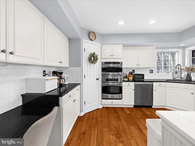 kitchen with sink, appliances with stainless steel finishes, hardwood / wood-style floors, tasteful backsplash, and white cabinets