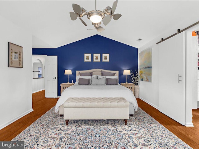 bedroom with hardwood / wood-style flooring, ceiling fan, lofted ceiling, and a barn door