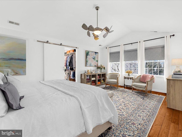 bedroom featuring ceiling fan, a spacious closet, vaulted ceiling, a barn door, and light wood-type flooring