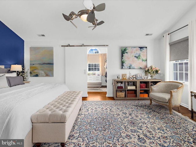 bedroom featuring hardwood / wood-style flooring, ensuite bath, a barn door, and ceiling fan