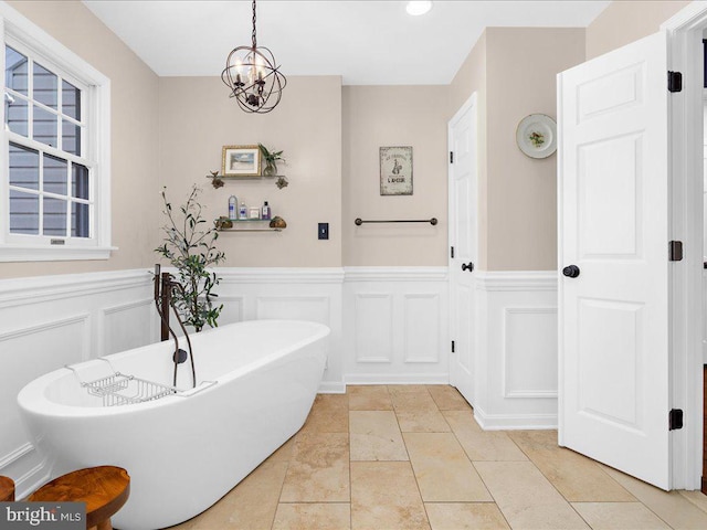 bathroom with a notable chandelier, tile patterned floors, and a tub to relax in