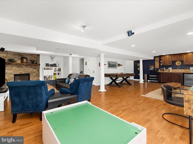 playroom with wine cooler, sink, a stone fireplace, and light hardwood / wood-style floors