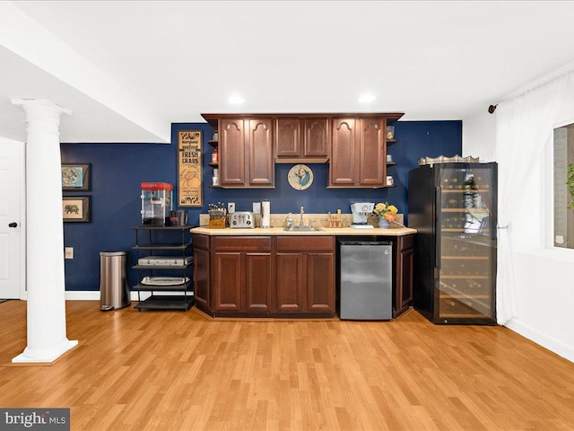 bar with ornate columns, black fridge, refrigerator, and light hardwood / wood-style flooring