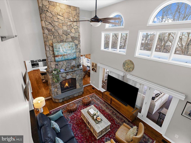 living room featuring hardwood / wood-style flooring, a stone fireplace, a towering ceiling, and ceiling fan