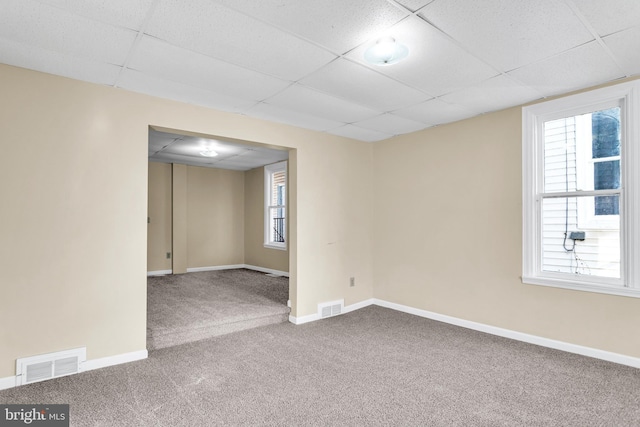 spare room featuring carpet flooring, a healthy amount of sunlight, and a drop ceiling