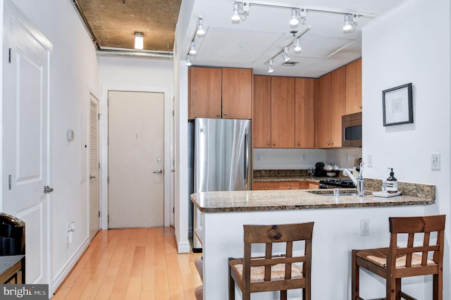 kitchen with sink, dark stone countertops, appliances with stainless steel finishes, kitchen peninsula, and light hardwood / wood-style floors