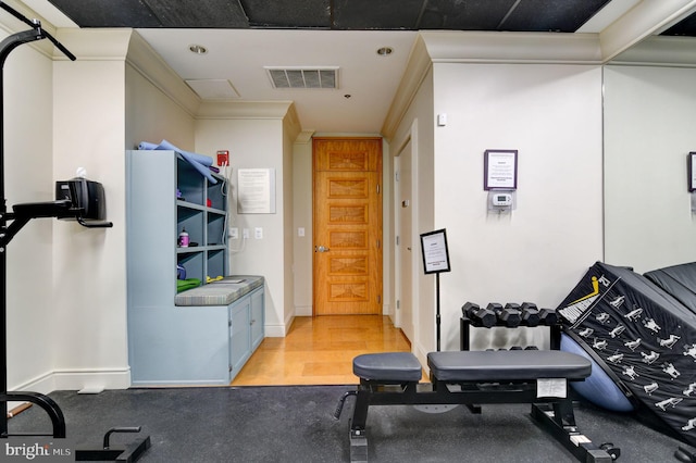 exercise area with baseboards, visible vents, and crown molding