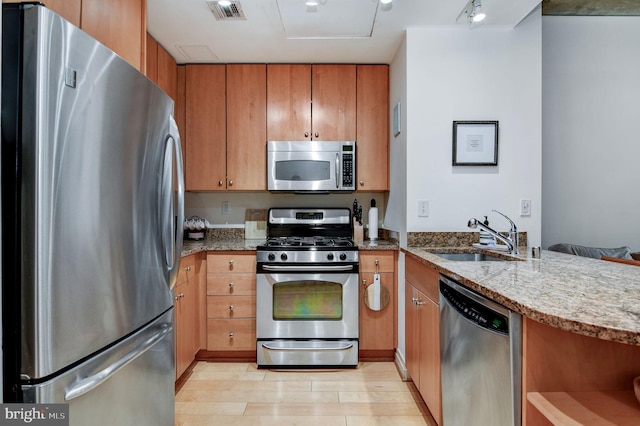 kitchen with sink, track lighting, light stone countertops, and appliances with stainless steel finishes