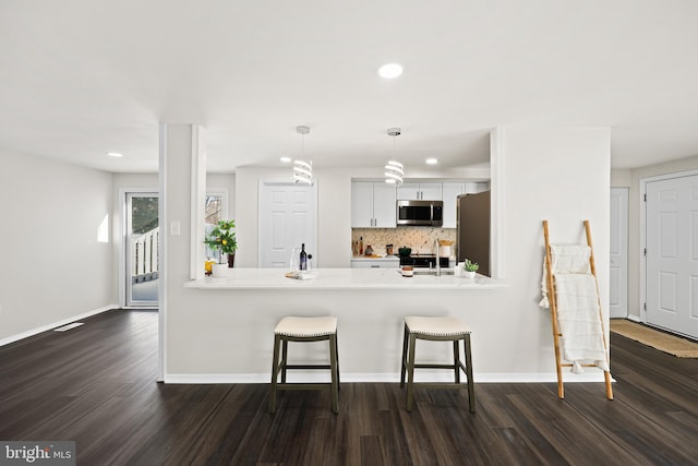 kitchen featuring pendant lighting, appliances with stainless steel finishes, white cabinetry, kitchen peninsula, and a breakfast bar