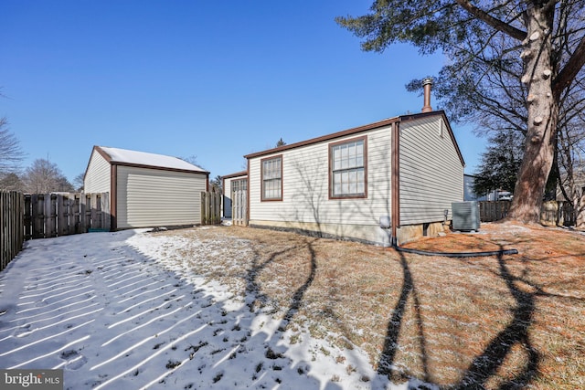 snow covered back of property featuring a garage, an outbuilding, and central AC unit