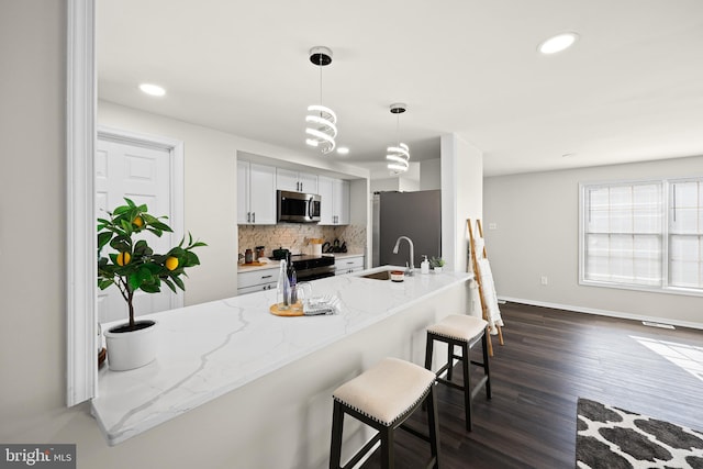 kitchen featuring stainless steel appliances, sink, hanging light fixtures, a kitchen breakfast bar, and light stone counters