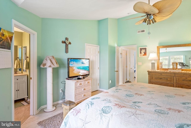 bedroom featuring ceiling fan, ensuite bath, light hardwood / wood-style floors, and a high ceiling