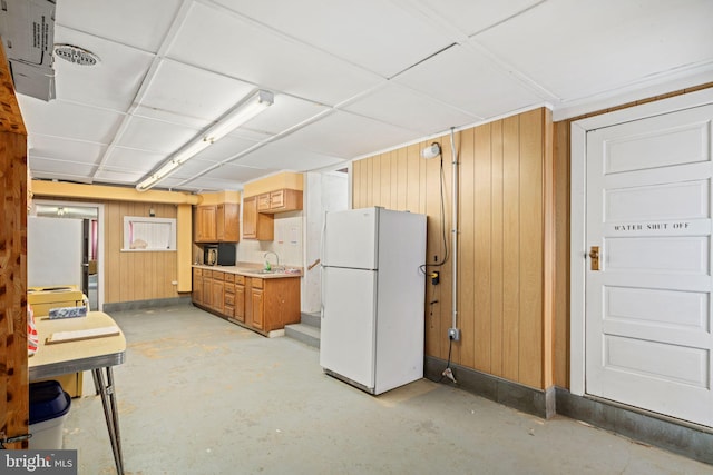 kitchen with sink, stainless steel fridge, wood walls, and white refrigerator