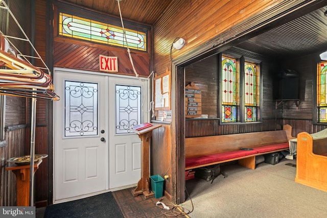 entrance foyer with carpet, french doors, wood ceiling, and wooden walls