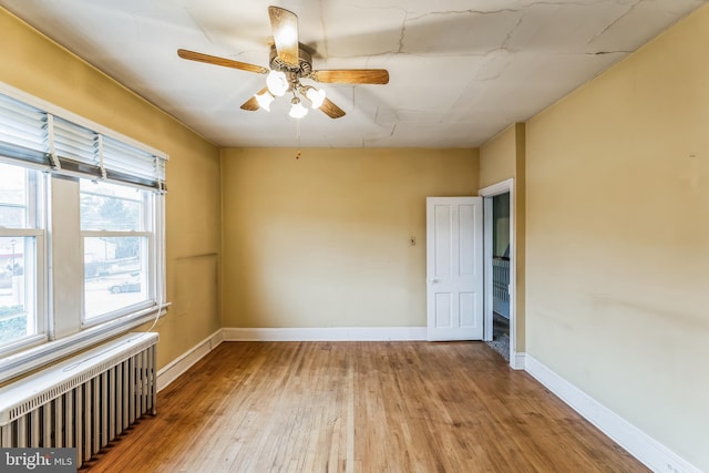 unfurnished room featuring radiator, ceiling fan, a wealth of natural light, and hardwood / wood-style flooring