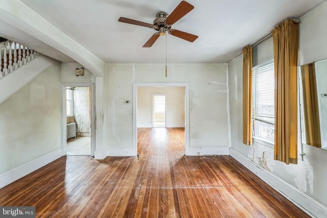 empty room with hardwood / wood-style flooring, radiator, ceiling fan, and a healthy amount of sunlight