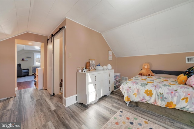 bedroom with hardwood / wood-style flooring, vaulted ceiling, and a barn door