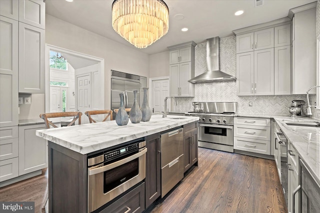 kitchen with sink, premium appliances, wall chimney exhaust hood, and a chandelier