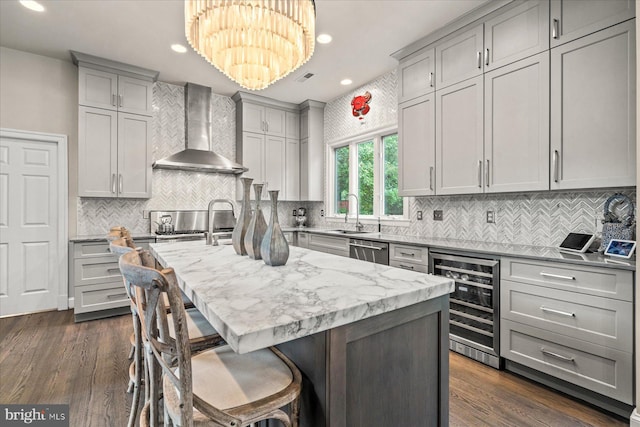 kitchen with an island with sink, decorative light fixtures, wine cooler, wall chimney exhaust hood, and stainless steel dishwasher