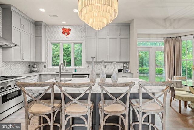 kitchen featuring stainless steel appliances, a kitchen island, a kitchen breakfast bar, a chandelier, and wall chimney exhaust hood