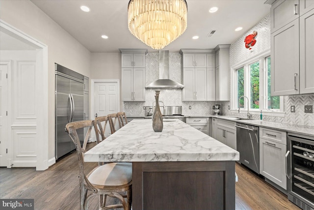 kitchen featuring decorative light fixtures, wine cooler, a center island, stainless steel appliances, and wall chimney exhaust hood