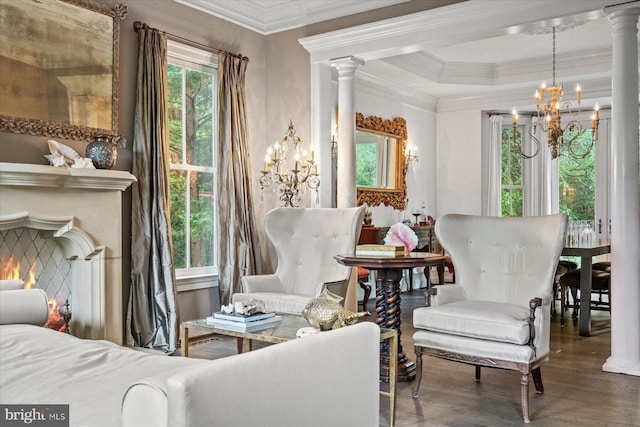 living area featuring ornate columns, ornamental molding, a chandelier, and hardwood / wood-style flooring