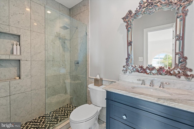 bathroom with toilet, tiled shower, and vanity