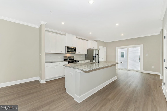 kitchen with an island with sink, stainless steel appliances, white cabinets, light stone countertops, and light hardwood / wood-style flooring