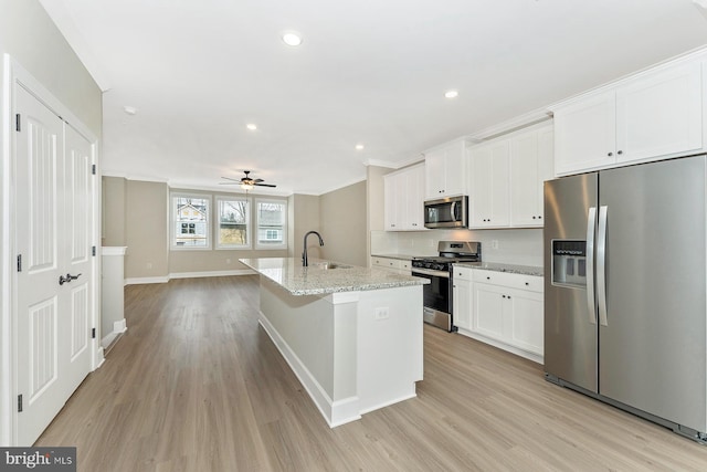 kitchen with ceiling fan, stainless steel appliances, white cabinetry, and a center island with sink