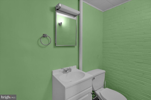 bathroom with vanity, crown molding, toilet, and brick wall