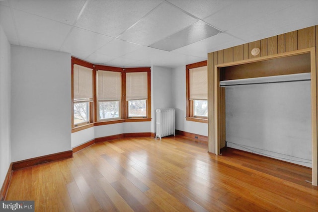 unfurnished bedroom with a paneled ceiling, radiator, hardwood / wood-style floors, and a closet