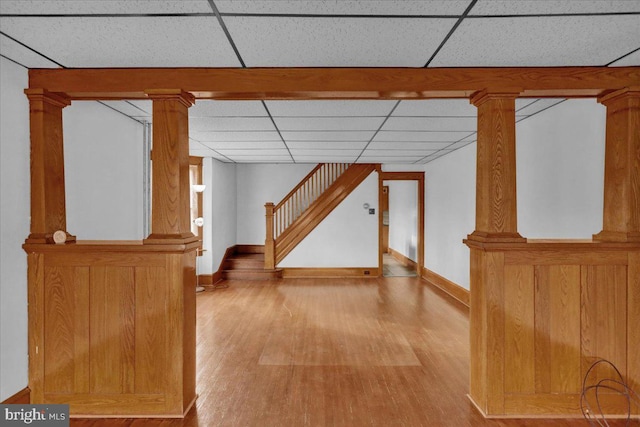 hallway with light wood-type flooring, a paneled ceiling, and ornate columns