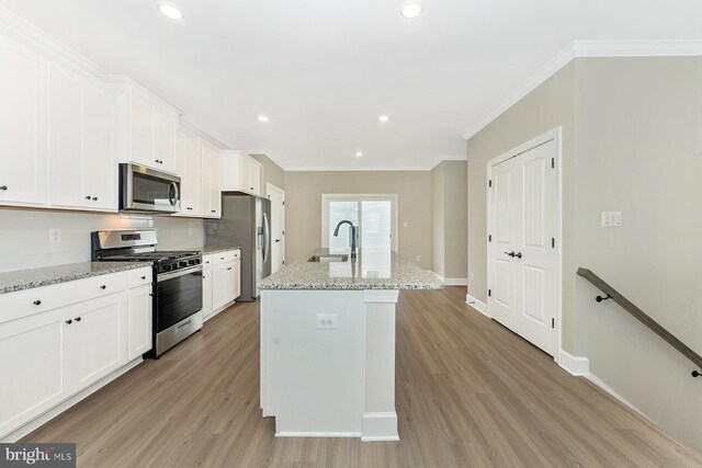 kitchen with decorative backsplash, light stone countertops, stainless steel appliances, and an island with sink