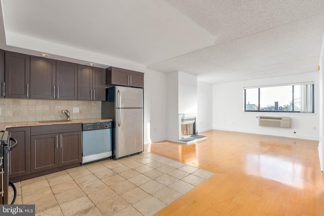 kitchen with a wall unit AC, stainless steel appliances, backsplash, dark brown cabinetry, and sink