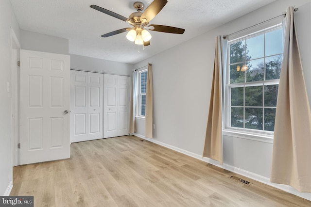 unfurnished bedroom featuring ceiling fan, light wood-type flooring, a closet, and multiple windows