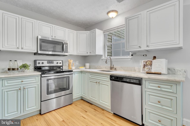 kitchen featuring light hardwood / wood-style floors, stainless steel appliances, a textured ceiling, white cabinets, and sink