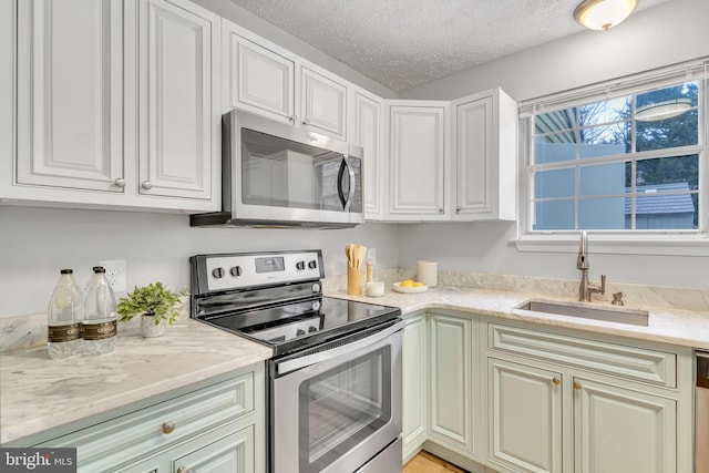 kitchen featuring a textured ceiling, white cabinetry, stainless steel appliances, sink, and light stone counters