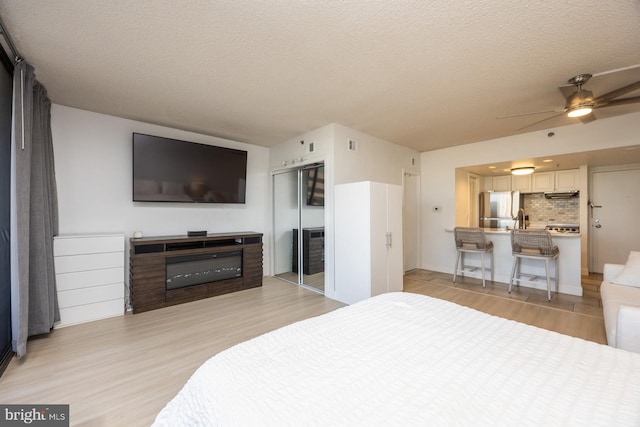 bedroom with ceiling fan, light hardwood / wood-style floors, stainless steel refrigerator, a textured ceiling, and a closet