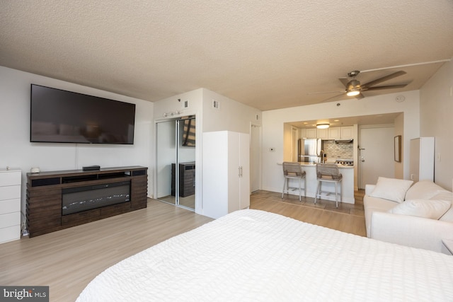 bedroom featuring ceiling fan, stainless steel refrigerator, a textured ceiling, and light hardwood / wood-style floors