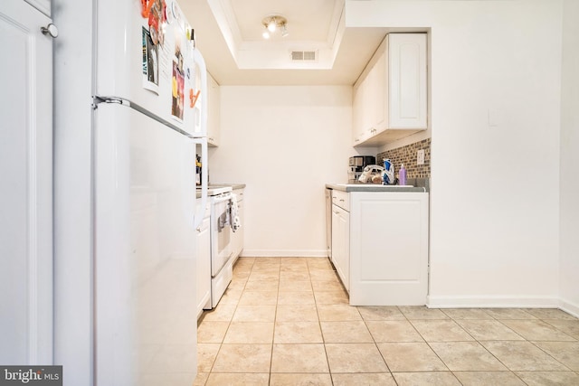 kitchen with a raised ceiling, decorative backsplash, light tile patterned flooring, white appliances, and white cabinets